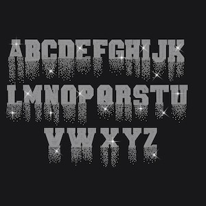 Puede incluir: Un alfabeto completo en mayúsculas, cada letra está hecha de pequeños y brillantes pedrería plateada. Las letras están dispuestas en tres filas sobre un fondo negro. El diseño tiene un efecto de goteo.