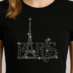 Op de afbeelding: Zwarte crop top met een strass ontwerp van de Eiffeltoren en het woord "PARIS". Het ontwerp is zilverkleurig. De top heeft korte mouwen en een ronde hals. Een populair kledingstuk.