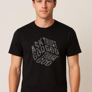 Puede incluir: Camiseta negra de manga corta con el texto "ASK TRUST GOD GOD THINK GOD" en una fuente brillante, similar a diamantes. El texto está dispuesto en un diseño geométrico estilizado.