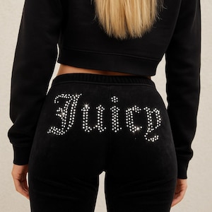 Può includere: Pantaloni della tuta in velluto nero con la scritta "Juicy" in strass scintillanti sul retro. I pantaloni della tuta hanno un girovita con coulisse. La modella indossa una felpa corta nera.