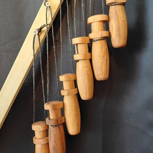 Pode incluir: Uma coleção de puxadores de gaveta de madeira, cada um com uma forma e padrão de grão únicos, suspensos por barbante de um suporte de madeira. Os puxadores variam em cor de castanho claro a escuro, criando uma estética natural e rústica.