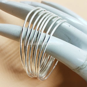 May include: A set of ten silver bangles stacked together. The bangles are thin and have a smooth, polished finish.