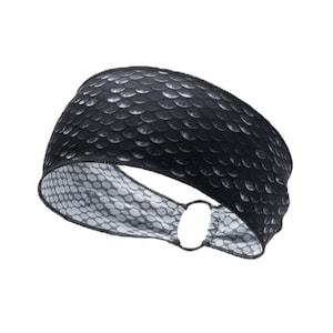 May include: Black headband with a textured, scale-like pattern on the exterior. The interior features a white and gray polka dot design. The headband has a circular opening on the side.