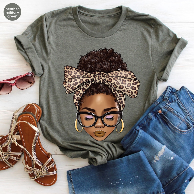 May include: A green t-shirt with a graphic of a woman with brown skin, brown hair, and closed eyes. She is wearing a leopard print headband and glasses.