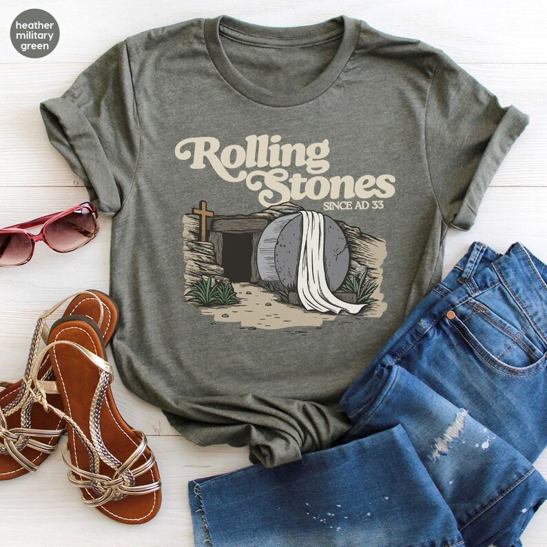 May include: Heather military green t-shirt with a graphic of a stone tomb with a white sheet draped over it. The text "Rolling Stones Since AD 33" is printed on the shirt.