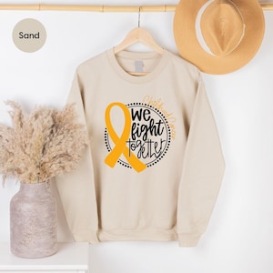 May include: Sand colored sweatshirt with a gold ribbon and the text "We fight together" in a black circle with the words "Childhood Cancer" above the circle.