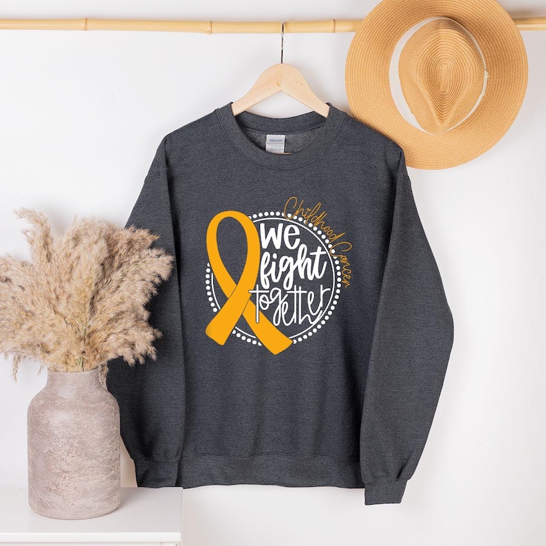 May include: A dark gray sweatshirt with a gold ribbon and the text "Childhood Cancer We Fight Together" in white.