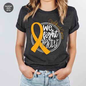 May include: Heather dark grey t-shirt with a gold ribbon and the text "Childhood Cancer We Fight Together" in a circle.
