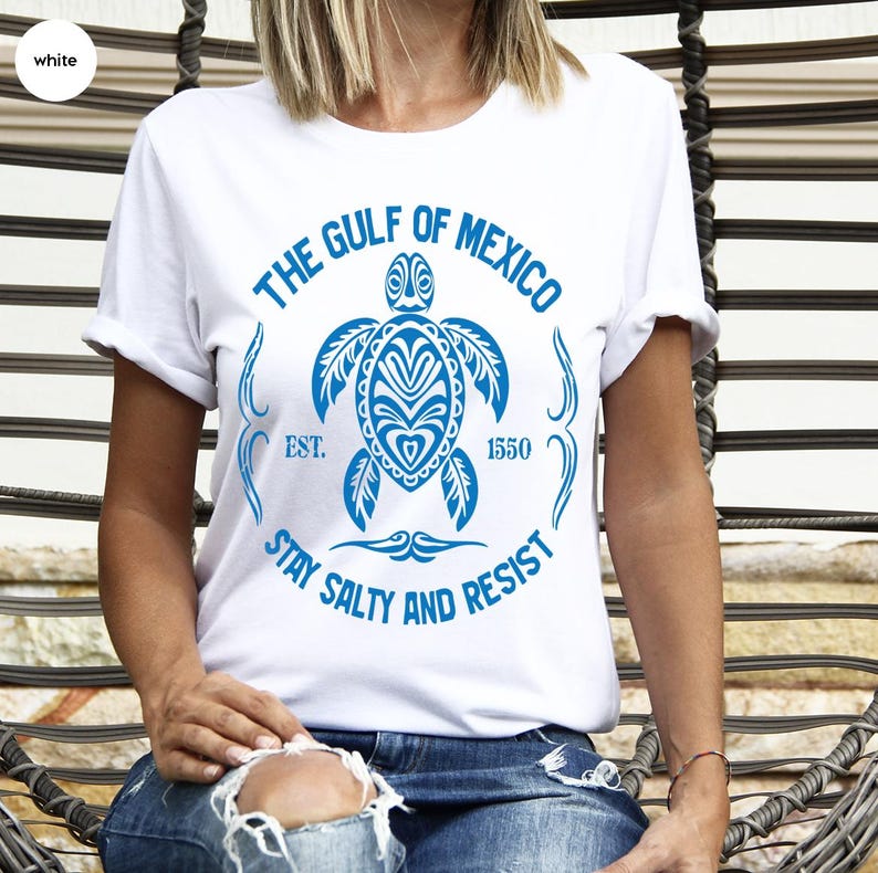 Puede incluir: Camiseta blanca con un gr&aacute;fico azul de una tortuga y el texto "The Gulf of Mexico Est. 1550 Stay Salty and Resist".