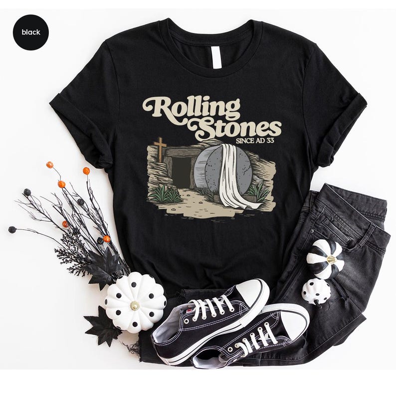 May include: Black t-shirt with a graphic of a stone tomb with a white sheet on top. The text "Rolling Stones Since AD 33" is above the tomb.