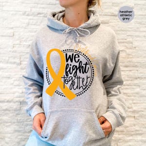 May include: Heather grey hoodie with a yellow ribbon and the text "We fight together" in a black circle.