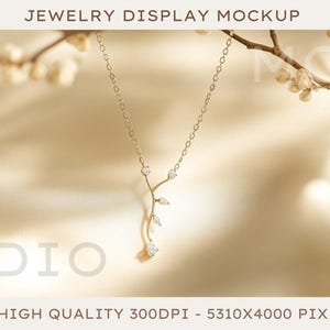 May include: A delicate gold necklace with a leaf design and small clear stones hangs from a branch against a light beige background. The necklace is a beautiful piece of jewelry that would make a great gift.