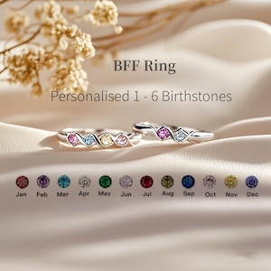 Może przedstawiać: Dwa srebrne pierścionki z kolorowymi kamieniami urodzeniowymi. Pierścionki są zaprojektowane tak, aby nosić je razem jako zestaw. Kamienie urodzeniowe są ułożone w rzędzie na każdym pierścionku. Kamienie urodzeniowe to: styczeń (czerwony), luty (fioletowy), marzec (niebieski), kwiecień (zielony), maj (szmaragdowo zielony), czerwiec (biały), lipiec (czerwony), sierpień (zielony), wrzesień (niebieski), październik (różowy), listopad (żółty) i grudzień (niebieski).