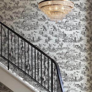 May include: A grand staircase with a black wrought iron railing and a patterned wallpaper featuring a black and white pastoral scene. A large crystal chandelier hangs above the stairs, and a potted plant sits at the base.
