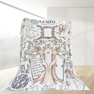 Può includere: Coperta bianca a tema Gemelli, con illustrazioni disegnate a mano. Presenta la parola "GEMINI" e le date "21 maggio-20 giugno". Include disegni di figure, fiori e simboli astrologici. La coperta è drappeggiata.