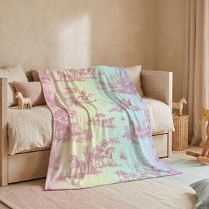 May include: A pastel-coloured blanket with a unicorn and landscape design draped over a bed. The blanket features a pink and white pattern on a gradient background of yellow, green, and blue. A wooden rocking horse and toy horses are nearby.