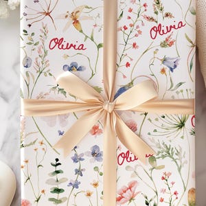 May include: A white gift box with a floral pattern and the name "Olivia" repeated four times. The box is tied with a beige satin ribbon.