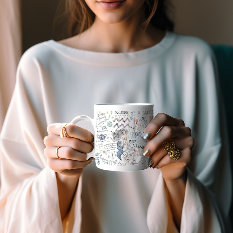 May include: White ceramic mug with a colorful illustration of an Aquarius zodiac sign. The illustration includes a mermaid, stars, and the text "Born to Envision".