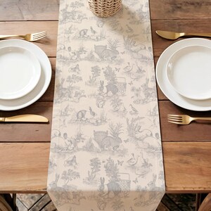 a table setting with a table runner featuring a pattern of rabbits and other animals, placed between two white plates and two gold forks.