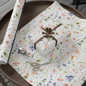 May include: White gift wrap with a watercolor floral pattern featuring pink, blue, and yellow flowers. A brown ribbon is tied around a white gift box.