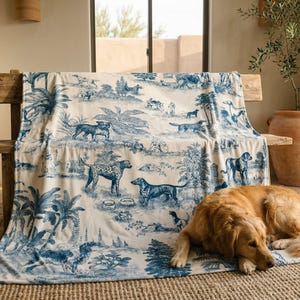 A golden retriever dog is lying on a rug in a room with a large blue and white patterned blanket featuring various animals and landscapes.