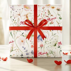 May include: A white gift box with a red ribbon and bow. The box is wrapped in floral patterned paper with the name "Olivia" written on it in red.