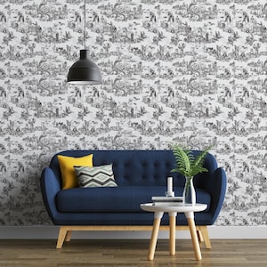 May include: Black and white Halloween-themed wallpaper featuring a repeating pattern of spooky scenes with skeletons, pumpkins, and bats. A blue sofa with yellow and patterned pillows sits in front of the wallpaper. A small white table and a fern in a vase are also in the image.