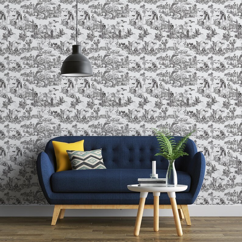 May include: Black and white Halloween-themed wallpaper featuring a repeating pattern of spooky scenes with skeletons, pumpkins, and bats. A blue sofa with yellow and patterned pillows sits in front of the wallpaper. A small white table and a fern in a vase are also in the image.