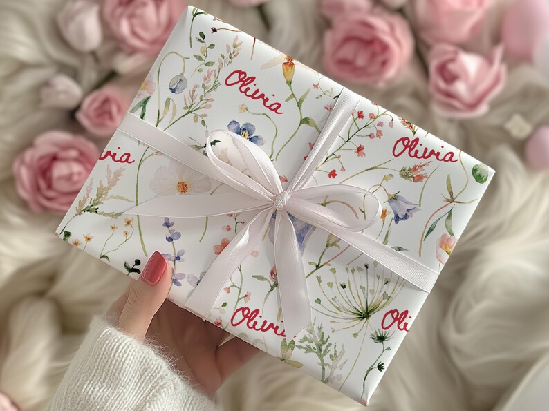 May include: White gift wrap with a floral pattern and the name "Olivia" repeated throughout. The wrap is tied with a white satin ribbon.