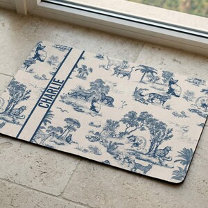 A decorative mat with a blue and white pattern featuring various animals and scenes, placed on a tiled floor near a window.
