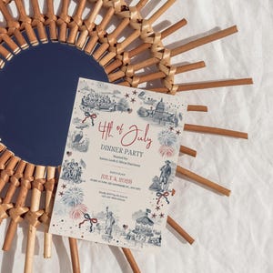 May include: A decorative 4th of July dinner party invitation with a vintage design, featuring illustrations of historical figures and landmarks. The invitation is placed on a woven sunburst mirror with a navy blue center.