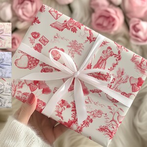 Pu&ograve; includere: Una scatola regalo bianca con un design a fantasia rosso e bianco. La scatola &egrave; legata con un nastro bianco e un fiocco. Il motivo presenta cuori, fiori e altri motivi romantici.