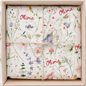 May include: A white gift box with a floral pattern and the name "Olivia" written in red on the wrapping paper. The box is tied with a brown twine.