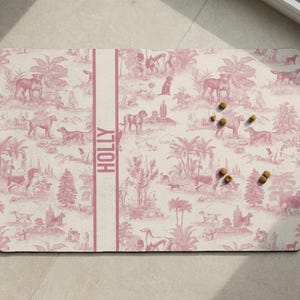 a pink and white patterned mat with various animal illustrations, including horses, dogs, and palm trees, arranged on a light-colored surface.