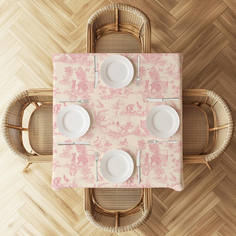 a table set for four with white plates, silverware, and a pink tablecloth featuring a pastoral scene. The table is surrounded by four wicker chairs, and the arrangement of the table and chairs suggests a formal dining setup.