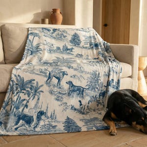 A dog is lying on the floor next to a couch, with a blue and white patterned blanket draped over the couch.