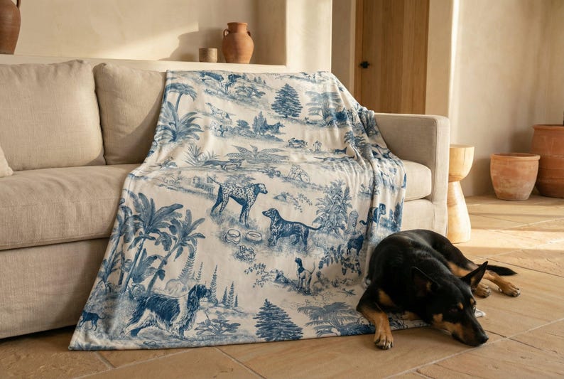 A dog is lying on the floor next to a couch, with a blue and white patterned blanket draped over the couch.