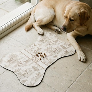 A golden retriever dog is lying on a tiled floor next to a bone-shaped dog food dish with animal illustrations.