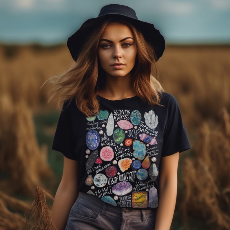 Puede incluir: Una camiseta negra con un estampado colorido de varios cristales y piedras preciosas. El estampado incluye los nombres de los cristales y sus significados asociados, como "curaci&oacute;n con malaquita", "intuici&oacute;n de iolite", "mis cristales curativos", "armon&iacute;a turquesa", "sabidur&iacute;a de amatista" y "ojo de tigre intr&eacute;pido".