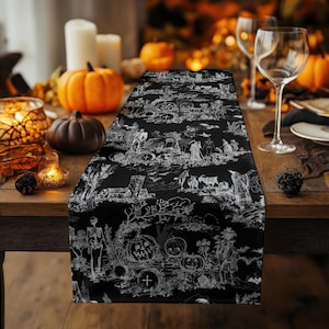 May include: Black and white Halloween-themed table runner featuring a toile design with pumpkins, skeletons, and other spooky illustrations. The runner is displayed on a wooden table, creating a festive and decorative centerpiece for a Halloween gathering.