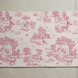May include: A rectangular placemat in pink and white, decorated with a toile de Jouy design. The pattern depicts various animals, trees, and buildings. The design includes tigers, cats, and other wildlife in a jungle setting.