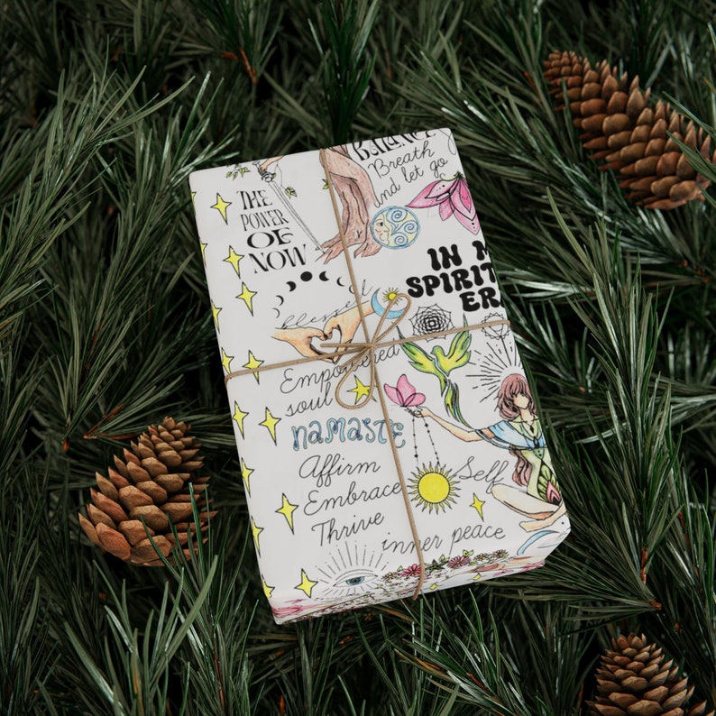 May include: A white gift box wrapped in paper with colorful illustrations and text, including "The Power of Now", "Breath and let go", "In My Spirit", "namaste", "Affirm", "Embrace", "Thrive", and "Inner Peace".