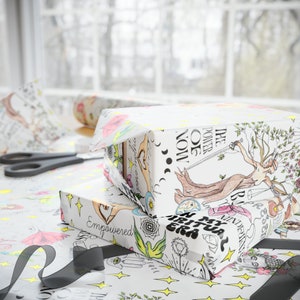 May include: Two gift boxes wrapped in white paper with colorful illustrations. The top box features a woman holding a sword and a tree with the text "The Power Of Now". The bottom box features a variety of illustrations including a hand with the text "Empowered".