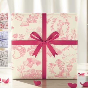 Pu&ograve; includere: Una scatola regalo bianca con un motivo floreale rosa e bianco &egrave; avvolta da un nastro rosa acceso. La scatola &egrave; appoggiata su un tavolo con cuori rosa sparsi intorno.