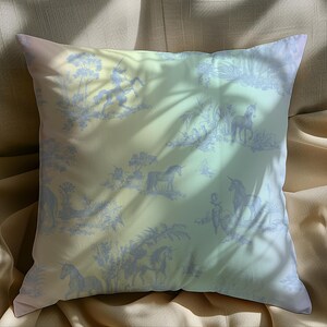 May include: Square cushion with a pastel gradient background and a blue toile pattern featuring unicorns, trees, and figures. The cushion is on a beige fabric, with shadows cast across the surface.