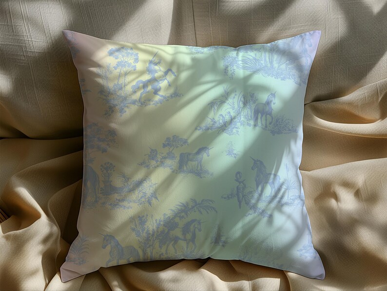 May include: Square cushion with a pastel gradient background and a blue toile pattern featuring unicorns, trees, and figures. The cushion is on a beige fabric, with shadows cast across the surface.