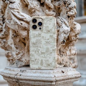 Op de afbeelding: Een witte iPhone-hoes met een beige en bruin patroon van bomen en dieren. De hoes heeft een uitsparing voor de camera en een gouden rand.