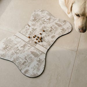 A dog is sitting on a tiled floor next to a large bone-shaped dog toy, which has several dog treats scattered on it.