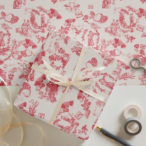 Pu&ograve; includere: Una scatola regalo bianca avvolta in carta a motivi rossi e bianchi con un nastro bianco. La carta presenta un motivo ripetitivo di cuori, fiori e coppie in un'ambientazione romantica. La scatola &egrave; appoggiata su una superficie bianca con forbici, nastro adesivo e una penna.