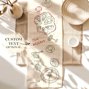 May include: A beige table runner with hand-drawn illustrations of food and kitchen items. The text "The Millers" is written in red. A plate, cup, and decorative vase are also visible.